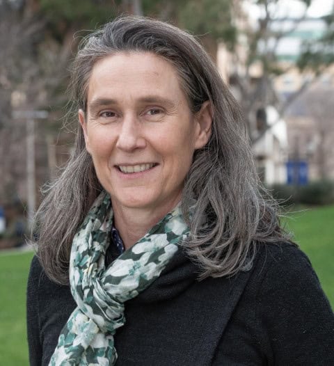 Skilled female soil scientist smiling outdoors with urban background, promoting soil health and sustainability.