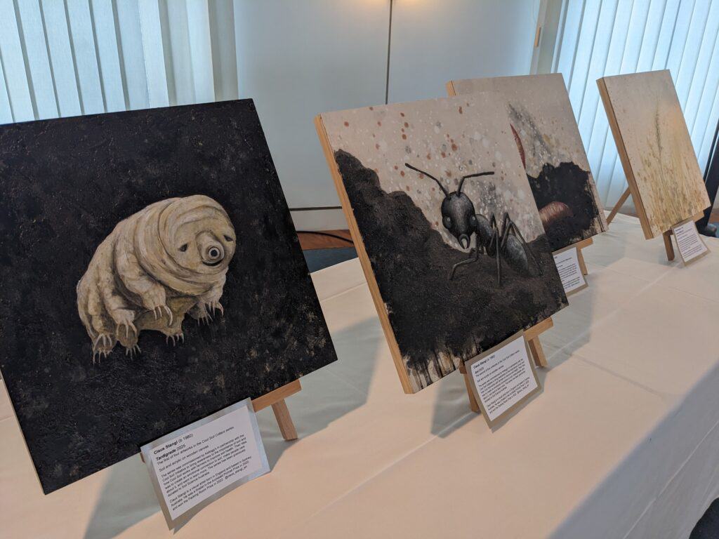 Acrylic paintings of soil-dwelling creatures displayed on wooden easels at a Soil Science Australia exhibition.